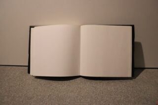 Ein offenes Buch mit leeren Seiten liegt auf einer strukturierten Oberfläche vor einem schlichten Hintergrund.