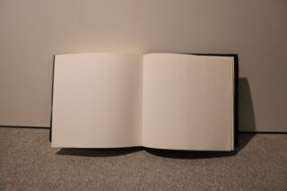 Ein offenes Buch mit leeren Seiten liegt auf einer grauen Fläche vor einem schlichten Hintergrund.
