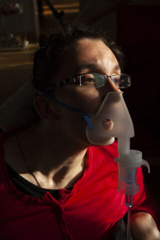 Eine Person mit Brille und rotem Hemd verwendet eine Verneblermaske und Licht scheint auf ihr Gesicht.