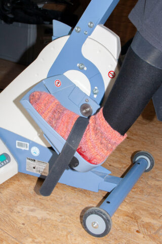 Eine Person in rosa Strickpantoffeln und schwarzen Strumpfhosen benutzt ein Heimtrainer-Fahrrad.