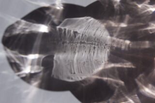 Abstrakte Formen und Lichtreflexionen erzeugen auf einer glatten Oberfläche ein Muster mit hellen und dunklen Bereichen und wellenförmigen, verzerrten Linien.