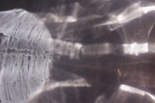 Abstrakte Lichtreflexionen und Schatten auf einer metallischen oder reflektierenden Oberfläche, die ein Muster aus hellen und dunklen Bereichen erzeugen.