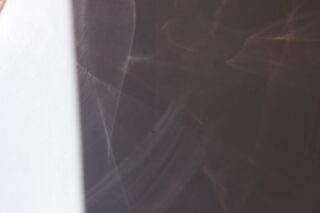 Links ist ein weißer vertikaler Streifen zu sehen, rechts befinden sich abstrakte Licht- und Schattenmuster auf einer bräunlich-grauen Fläche.