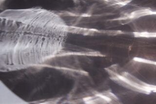 Abstraktes Muster aus Licht und Schatten mit wellenförmigen, reflektierenden Linien und verschwommenen Formen auf einer glatten, metallischen Oberfläche.