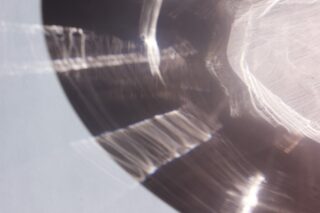 Nahaufnahme von Lichtreflexionen und -brechungen auf einer gewölbten Metall- oder Glasoberfläche, die helle Muster und Linien auf einen glatten Hintergrund werfen.