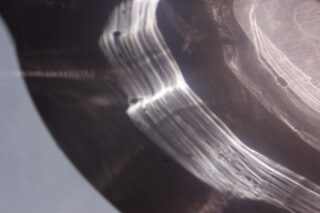 Abstrakte Nahaufnahme von gekrümmten Lichtreflexionen und Schatten auf einer glatten, möglicherweise metallischen Oberfläche mit einigen sichtbaren kleinen dunklen Flecken.