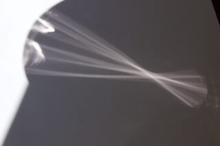 Ein weiches, abstraktes Muster aus weißen Lichtstrahlen wird auf eine glatte graue Oberfläche projiziert, wodurch ein fächerartiger Effekt mit unscharfen Rändern entsteht.