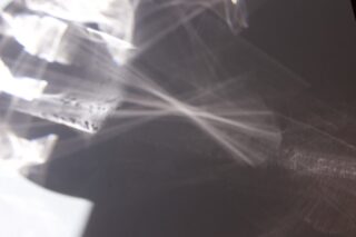 Abstraktes Muster aus Licht und Schatten mit sich kreuzenden Linien und sanften Farbverläufen auf einer blassen Oberfläche.