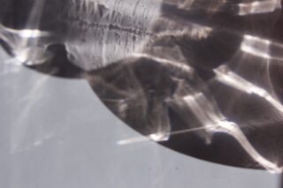 Abstrakte Nahaufnahme von Lichtreflexionen und Schatten auf einer Metall- oder Glasoberfläche, die geschwungene und lineare Muster vor einem neutralen Hintergrund erzeugt.