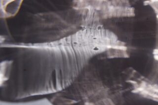 Nahaufnahme abstrakter, unscharfer Lichtmuster und Schatten auf einer durchscheinenden Oberfläche, die Streifen, Flecken und weiche Farbverläufe in Grau- und Weißtönen erzeugen.