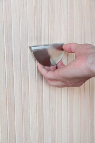 Eine Hand greift nach einem halbmondförmigen Metallgriff auf einer hellen Holzoberfläche.