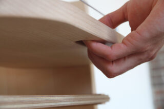 Eine Hand öffnet eine Holzschublade, indem sie einen eingekerbten Griff an der Unterseite der Schubladenfront greift.