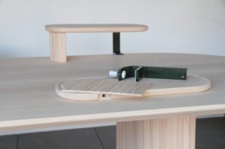 Ein heller Holztisch mit einer kleinen erhöhten Plattform und einer Metallhalterung, die oben eine verstellbare Holzlattenoberfläche hält.