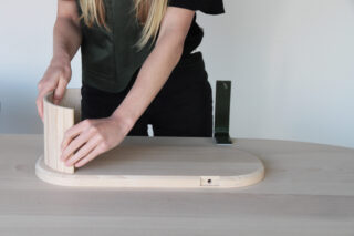 Eine Person montiert ein helles Holzstück auf einem abgerundeten Holzsockel auf einem hellen Tisch.