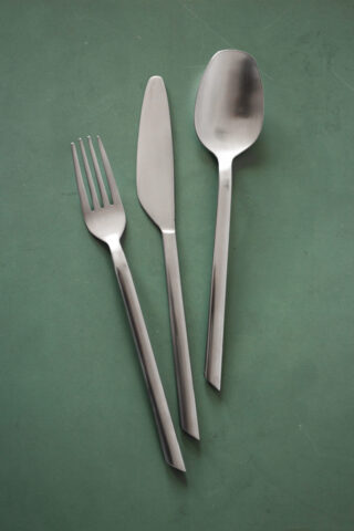 Eine Gabel, ein Messer und ein Löffel aus Edelstahl sind nebeneinander auf einer grünen Oberfläche angeordnet.