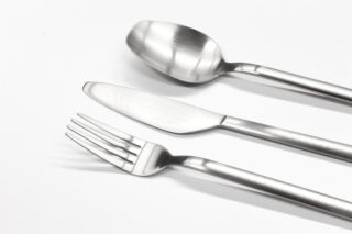 Ein Löffel, ein Messer und eine Gabel aus Edelstahl sind nebeneinander auf einem weißen Hintergrund angeordnet.