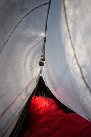 Innenansicht eines Zeltes mit einem roten Schlafsack und einer kleinen Hängelaterne, wobei Licht durch den Zeltstoff fällt.