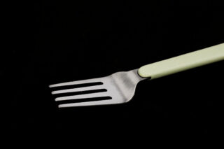 Vor einem schwarzen Hintergrund ist eine Metallgabel mit hellgrünem Griff positioniert.