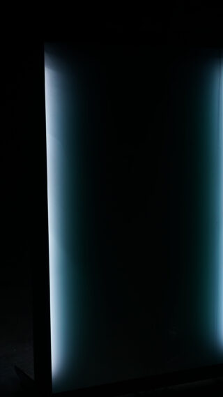 Ein vertikales rechteckiges Panel mit einem schwachen blauen Schimmer an den Rändern vor einem dunklen Hintergrund.