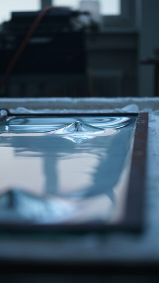 Nahaufnahme eines rechteckigen Tabletts, gefüllt mit stillem Wasser, mit Wellen und einer kleinen Spitze in der Mitte, mit unscharfem Hintergrund.