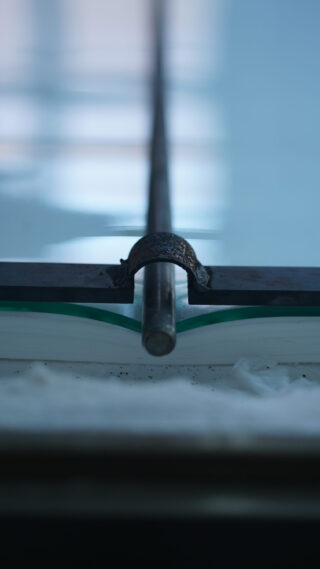 Nahaufnahme einer Metallstange mit einer Klammer, die auf der Kante eines Stapels weißen Papiers ruht, mit einem unscharfen blauen Hintergrund.