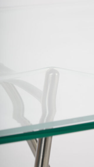 Eine Nahaufnahme einer Tischplatte aus klarem Glas, die von Metallbeinen getragen wird, vor einem schlichten weißen Hintergrund.