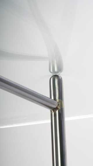 Nahaufnahme von zwei in einem Winkel verbundenen Metallstäben, wobei ein Stab vor einem schlichten, hellen Hintergrund in Bewegung zu sein scheint.