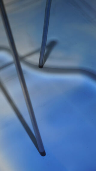 Zwei Metallbeine eines Stuhls oder Tisches werfen Schatten auf eine glatte blaue Oberfläche.