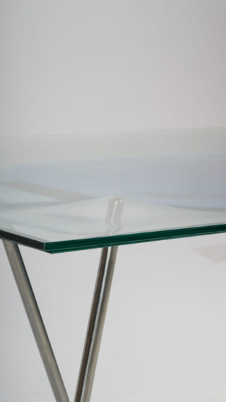 Eine Nahaufnahme eines Glastisches mit Metallrahmen und -beinen, aus einem Winkel vor einem schlichten hellen Hintergrund gezeigt.