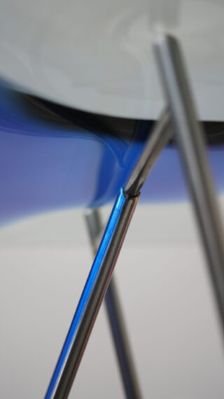 Nahaufnahme sich kreuzender Stuhlbeine aus Metall mit einer Teilansicht einer blauen Sitzfläche und einem unscharfen weißen Hintergrund.