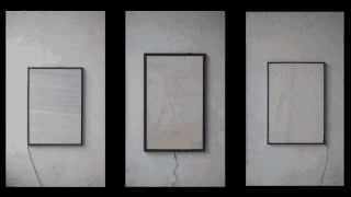 Drei rechteckige Rahmen mit dezenten Mustern hängen an einer strukturierten weißen Wand; an jedem Rahmen hängt sichtbar ein schwarzes Stromkabel herunter.