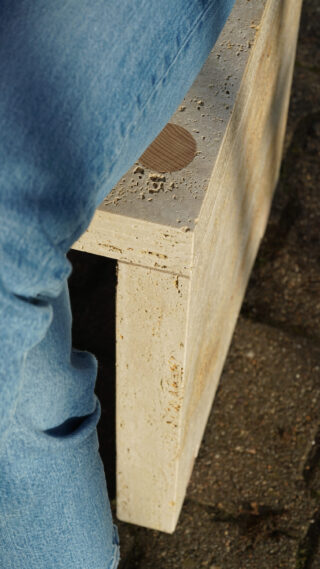 Person in Blue Jeans sitzt auf einer hellen, strukturierten Steinbank, wobei ein Teil ihres Beins und die Bankoberfläche sichtbar sind.