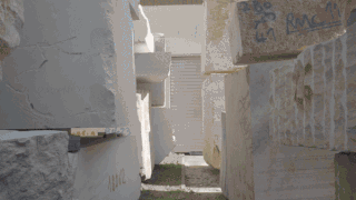 Große rechteckige Marmorblöcke sind im Freien in Reihen gestapelt. Das Sonnenlicht wirft Schatten zwischen ihnen und auf den Steinoberflächen sind einige Graffiti und Zahlen sichtbar.