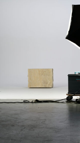 In der Mitte eines Fotostudios steht ein Steinblock, im Vordergrund sind Beleuchtungsgeräte und Kabel zu sehen.