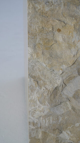 Nahaufnahme der Ecke einer strukturierten, beigen Stein- oder Felsoberfläche mit einem glatten, hellen Hintergrund auf der linken Seite.