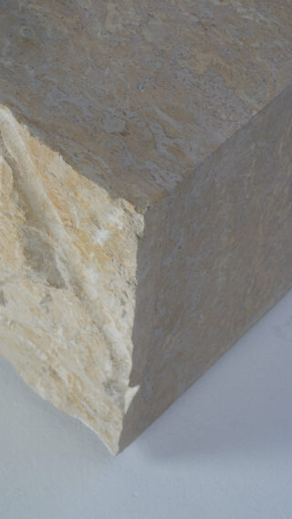 Nahaufnahme der Ecke eines großen Steinblocks mit rauer Textur, der auf einer hellen Oberfläche liegt.