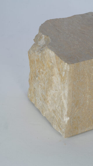 Ein großer, rauer, beiger Stein mit unebenen Kanten liegt auf einer hellgrauen Oberfläche.