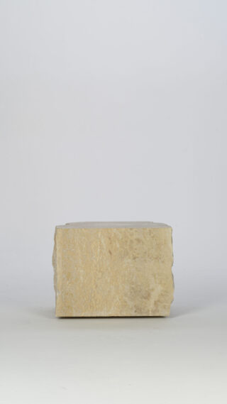Ein rechteckiger Block aus rauem beigem Stein liegt auf einem schlichten weißen Hintergrund.