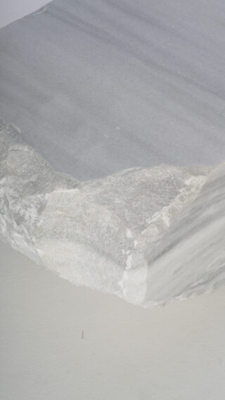 Eine Nahaufnahme einer Steinplatte mit rauer, unebener Kante und glatter, flacher Oberfläche.