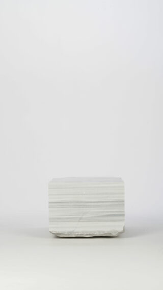 Ein rechteckiger Block aus hellgrauem Stein mit horizontalen Streifen liegt auf einem schlichten, hellen Hintergrund.