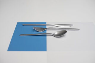 Drei Besteckteile – ein Messer, eine Gabel und ein Löffel – sind in einer Reihe auf einem gleichmäßig blau-weißen Hintergrund angeordnet.