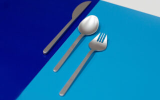 Ein Messer, ein Löffel und eine Gabel aus Edelstahl sind auf einer Oberfläche angeordnet, die in dunkelblaue und hellblaue Abschnitte unterteilt ist.