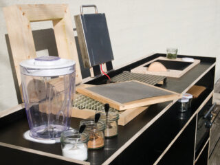 Eine Arbeitsplattenanordnung mit einem Wasserfilterkrug, Glasbehältern mit Löffeln, Holzrahmen, einem kleinen Solarpanel und anderen Werkzeugen, angeordnet für eine Demonstration oder ein Projekt.