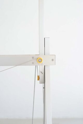 Minimalistische Nahaufnahme einer weißen Metallstruktur mit dünnen Kabeln und einem gelben kreisförmigen Element am Schnittpunkt der vertikalen und horizontalen Balken.