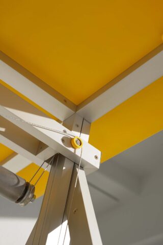 Nahaufnahme einer Metallstruktur mit einem Kabel- und Flaschenzugsystem vor einer gelben Deckenplatte.