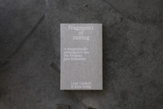 Auf einer strukturierten dunklen Oberfläche liegt ein graues Buch mit dem Titel „Fragmente des Bergbaus: Eine designspezifische Untersuchung der Sedimente der Schwäbischen Alb“ von Lenn Gerlach und Kyra Heilig.
