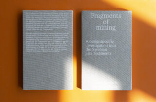 Zwei graue Hardcover-Bücher mit dem Titel „Fragments of Mining“ liegen auf einer orangefarbenen Oberfläche, eines mit der Vorderseite nach oben, sodass der Einband zu sehen ist, das andere umgedreht, sodass der Text auf der Rückseite zu sehen ist.