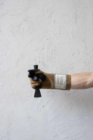 Eine behandschuhte Hand hält ein schwarzes Handwerkzeug vor einer strukturierten weißen Wand.