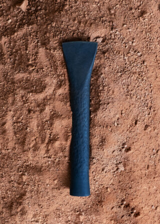 Ein strukturiertes, dunkel gefärbtes Metallwerkzeug oder -objekt liegt auf rotbraunem Schmutz.