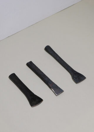Auf einer hellen Fläche sind drei schwarze Meißel aus Metall mit unterschiedlichen Klingenformen in einer Reihe angeordnet.